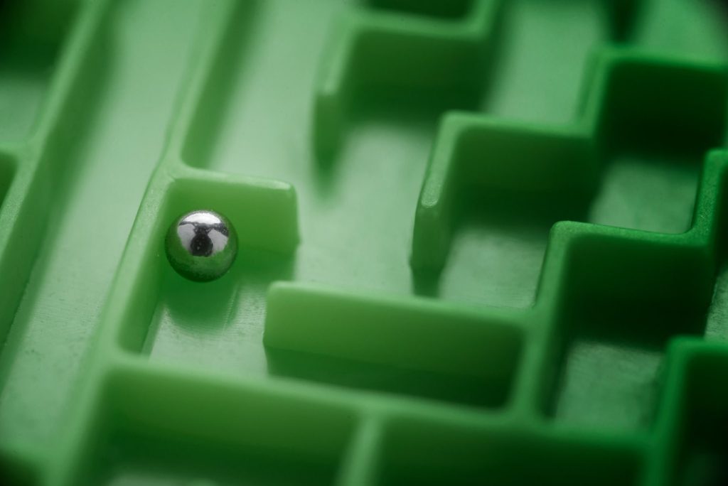 A metal ball navigating a green plastic maze, representing solving complex business problems